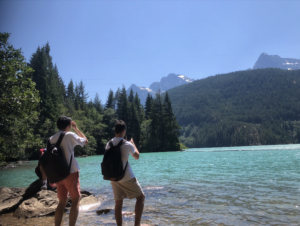 Students at the edge of the small beach at Diablo Lake taking pictures of the amazing blue green lake and mountains in the background.